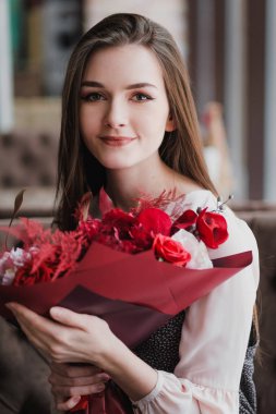 Kız bir buket kırmızı çiçek, peonies, gül ve Kasımpatı ile bir kafede oturuyor.