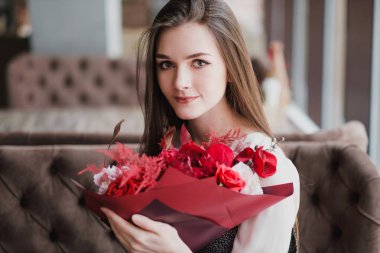 Kız bir buket kırmızı çiçek, peonies, gül ve Kasımpatı ile bir kafede oturuyor.