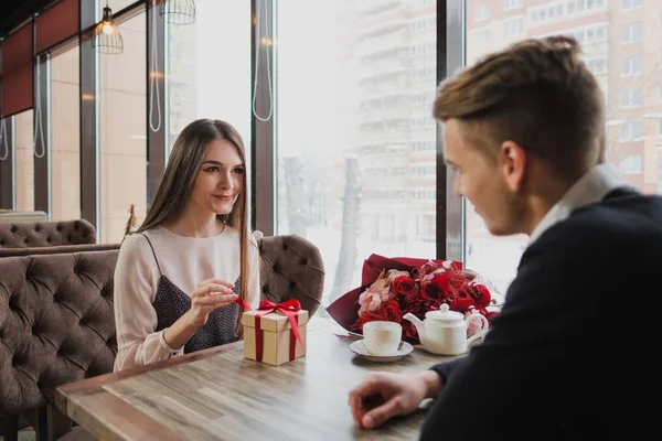 Genç bir adam bir kıza, eşi, pencere kenarındaki bir kafede bir hediye bir kırmızı kurdele ile verir.