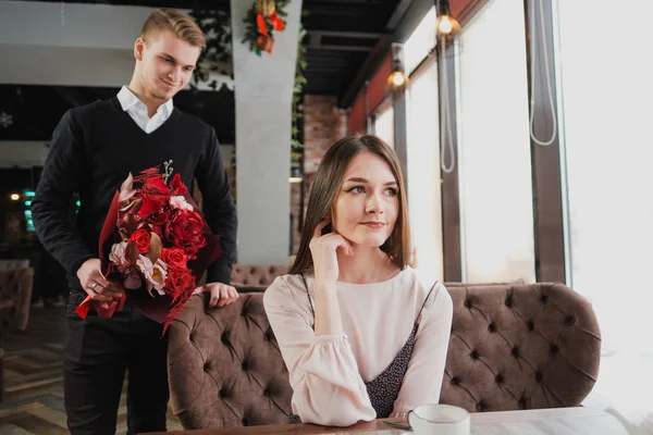 Genç bir adam arkadaşına, karısı, pencere kenarındaki bir kafede bir buket kırmızı çiçek verir.