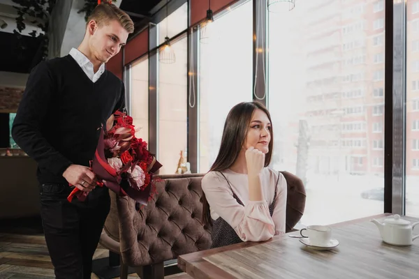 Genç bir adam arkadaşına, karısı, pencere kenarındaki bir kafede bir buket kırmızı çiçek verir.
