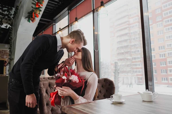 Genç bir adam arkadaşına, karısı, pencere kenarındaki bir kafede bir buket kırmızı çiçek verir. — Stok fotoğraf