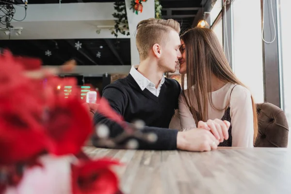 Młoda para w miłości, mężczyzna i kobieta na romantyczną randkę w kawiarni. Siedzą przy stoliku przy oknie. Na stole bukiet czerwonych kwiatów. — Zdjęcie stockowe