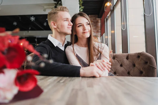 Genç çift sevgi, erkek ve kadın bir kafede romantik bir tarih. Pencerenin yanındaki bir masada oturmak. Masada bir buket kırmızı çiçek.