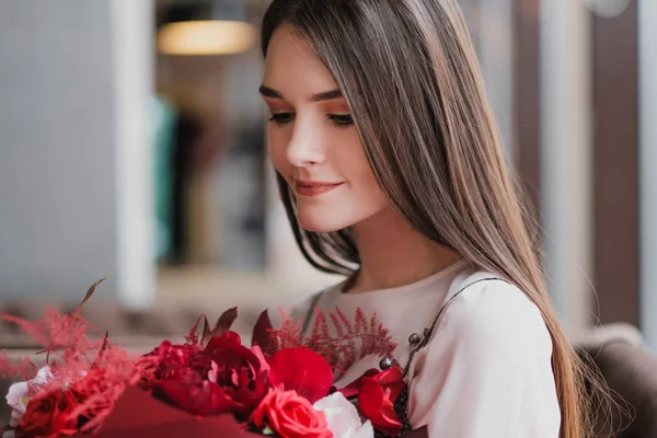 La ragazza è seduta in un caffè con un mazzo di fiori rossi, peonie, rose e crisantemi . — Foto Stock