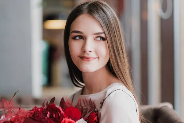 Дівчина сидить в кафе з букетом червоних квітів, півоній, троянд і хризантем . — стокове фото