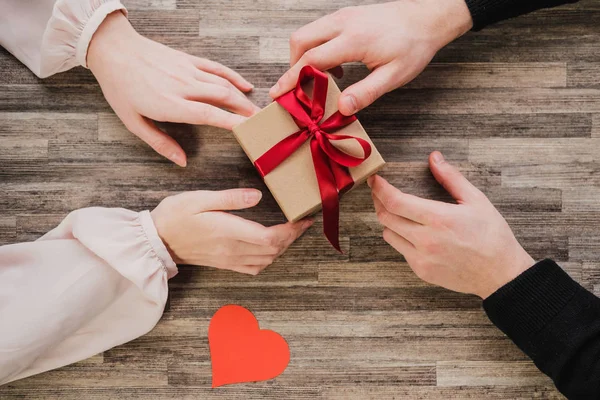 Вид сверху, подарочная коробка, мужские и женские руки, сердце Валентины, на фоне стола . — стоковое фото