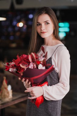 Kız bir buket kırmızı çiçek, peonies, gül ve Kasımpatı ile bir kafede oturuyor.