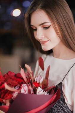 Kız bir buket kırmızı çiçek, peonies, gül ve Kasımpatı ile bir kafede oturuyor.