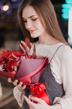 Kız bir buket kırmızı çiçek, peonies, gül ve Kasımpatı ile bir kafede oturuyor.