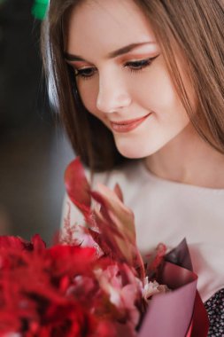 Kız bir buket kırmızı çiçek, peonies, gül ve Kasımpatı ile bir kafede oturuyor.