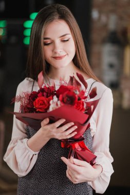 Kız bir buket kırmızı çiçek, peonies, gül ve Kasımpatı ile bir kafede oturuyor.