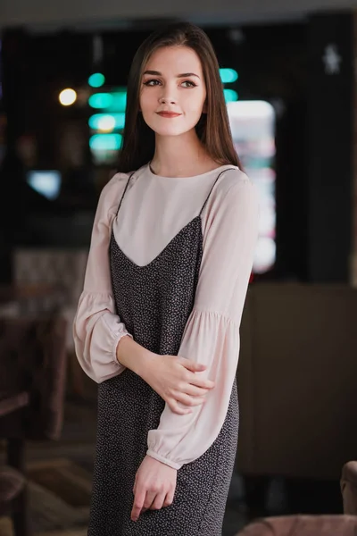 Portret młodej dziewczyny z długimi włosami na tle świetliste znaki we wnętrzu kawiarni lub restauracji. Czarną sukienkę i bluzkę, elegancki i atrakcyjny. — Zdjęcie stockowe