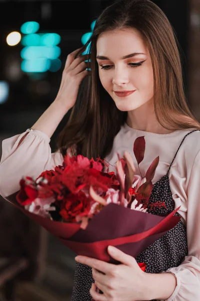 La chica está sentada en un café con un ramo de flores rojas, peonías, rosas y crisantemos . —  Fotos de Stock