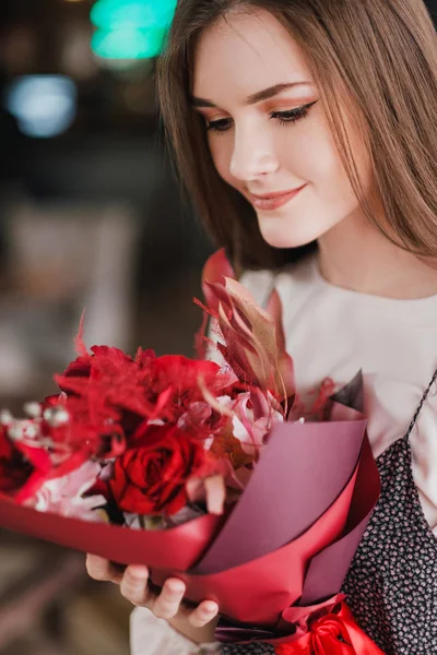 La chica está sentada en un café con un ramo de flores rojas, peonías, rosas y crisantemos . —  Fotos de Stock