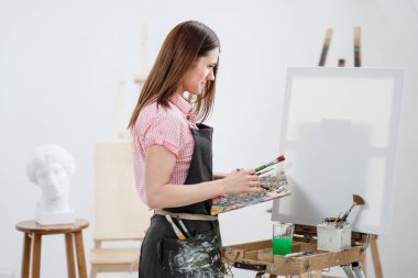 Bir genç kadın ressam parlak beyaz Studio bir şövale üzerinde tuval üzerine resim çizer.
