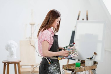 Bir genç kadın ressam parlak beyaz Studio bir şövale üzerinde tuval üzerine resim çizer.