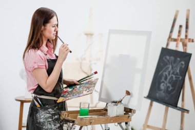 Bir genç kadın ressam parlak beyaz Studio bir şövale üzerinde tuval üzerine resim çizer.