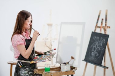 Bir genç kadın ressam parlak beyaz Studio bir şövale üzerinde tuval üzerine resim çizer.