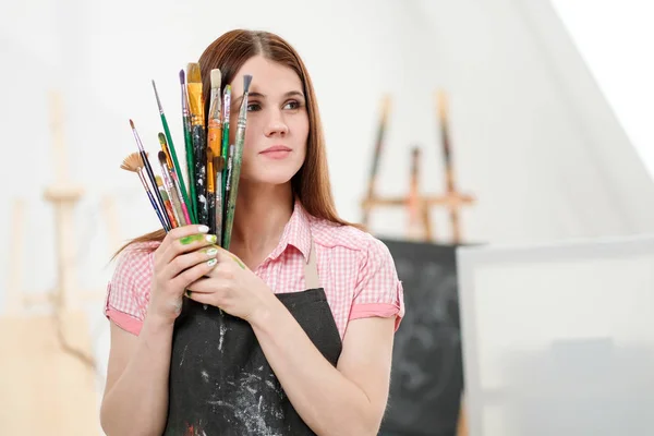 Jonge vrouw kunstenaar met penselen en verf in een witte studio. — Stockfoto