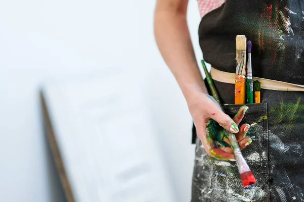 Woman artists hand with a brush and red paint. Black apron, white background.