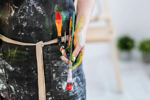 Woman artists hand with a brush and red paint. Black apron, white background.