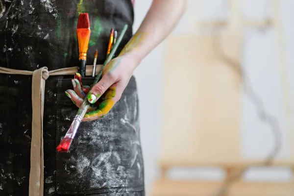 Kvinna konstnärer handen med en borste och röd färg. Svart förkläde, vit bakgrund. — Stockfoto