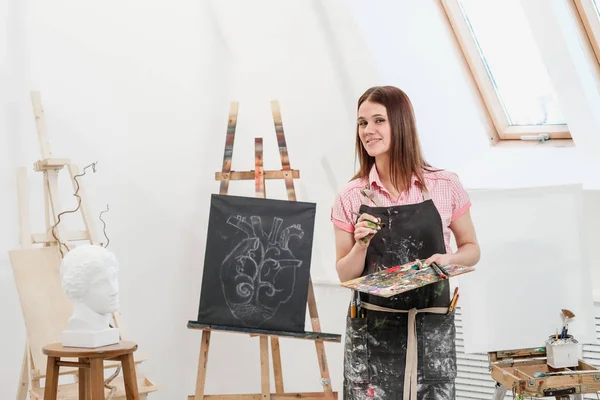 Молодая художница в яркой белой студии рисует картину на холсте на мольберте . — стоковое фото
