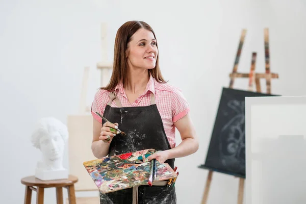 Молодая художница в яркой белой студии рисует картину на холсте на мольберте . — стоковое фото