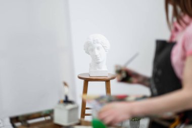 Genç güzel kız ressam beyaz bir stüdyoda bir şövale üzerinde tuval üzerinde çizer.