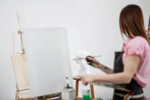 Joven hermosa niña pintor en un estudio blanco dibuja en un caballete sobre lienzo . —  Fotos de Stock