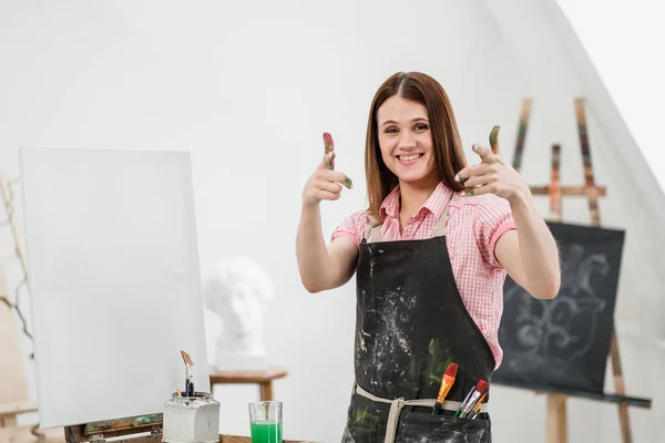 Młody piękny dziewczyna malarz w biały studio z brudne dłonie pokazuje klasę, śmieje się i raduje się. — Zdjęcie stockowe