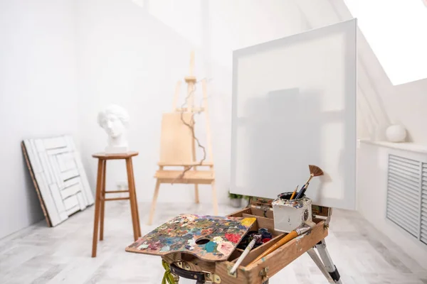 Interior del estudio blanco del artista, persona creativa. caballete, cepillos, cabeza de yeso y figuras. Ático, techos altos . — Foto de Stock