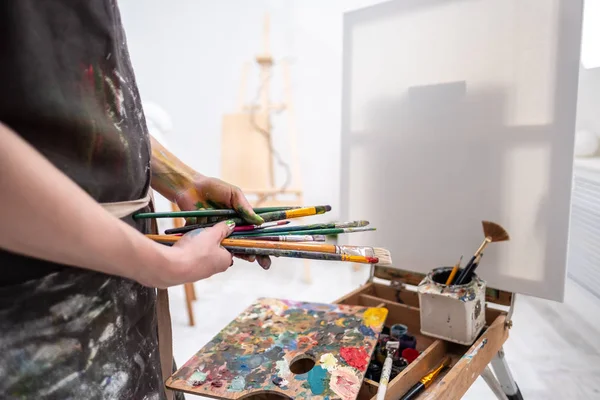 Giovane bella ragazza pittrice in uno studio bianco disegna su un cavalletto su tela . — Foto Stock