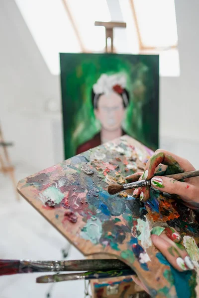 Young beautiful girl painter in a white studio draws on an easel on canvas.