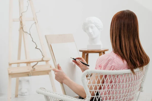 若い女性アーティストは 鉛筆をキャンバスに描画します 白いスタジオ ピンクのシャツにエプロン 図面や絵画レッスン プロのアーティスト — ストック写真