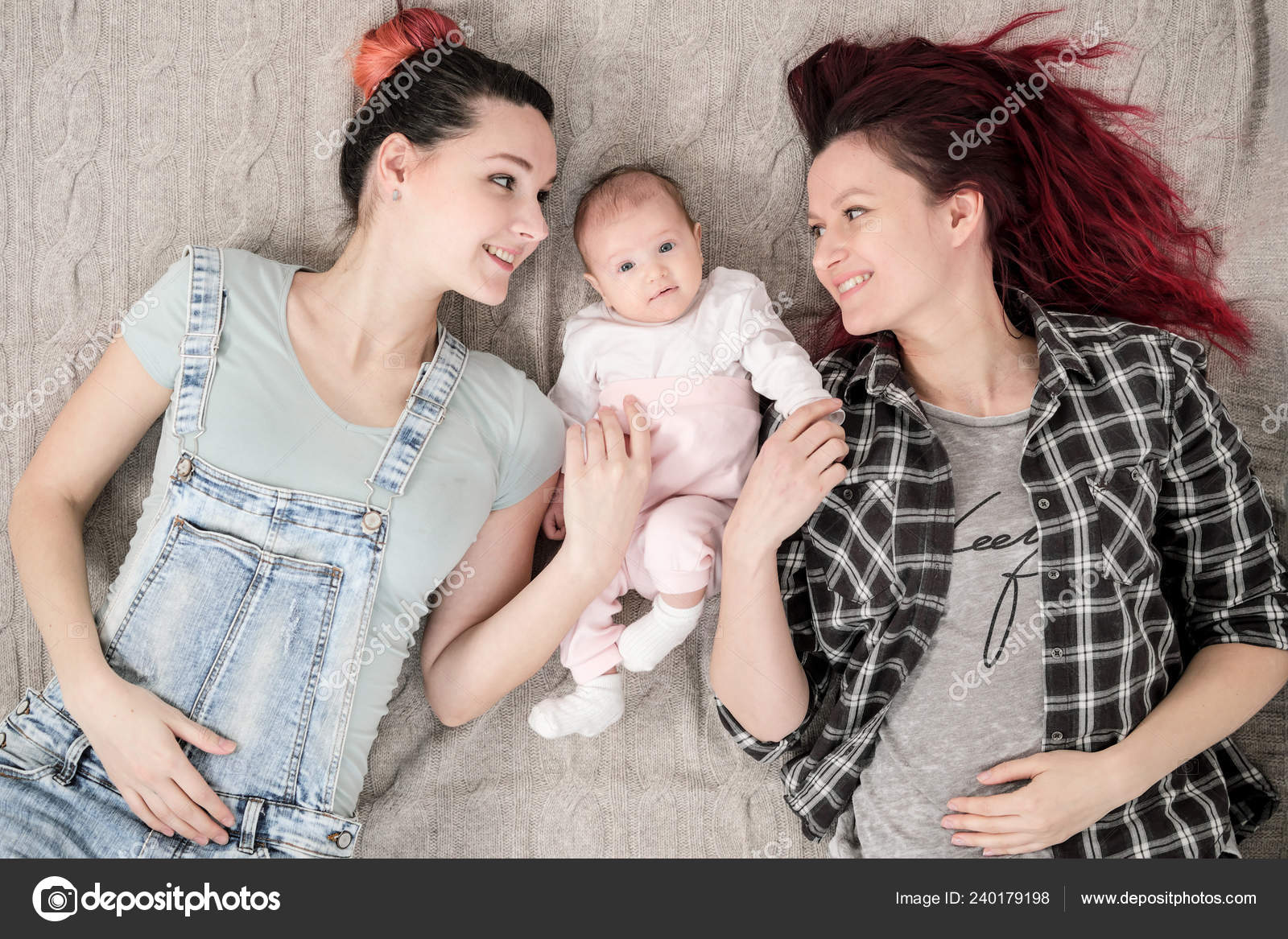 Two young women, a lesbian homosexual couple, are lying on a blanket with a child pic image