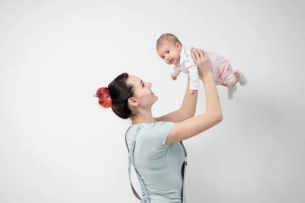 Giovane donna madre in tuta denim tiene un bambino in braccio. Sfondo bianco in studio . — Foto Stock