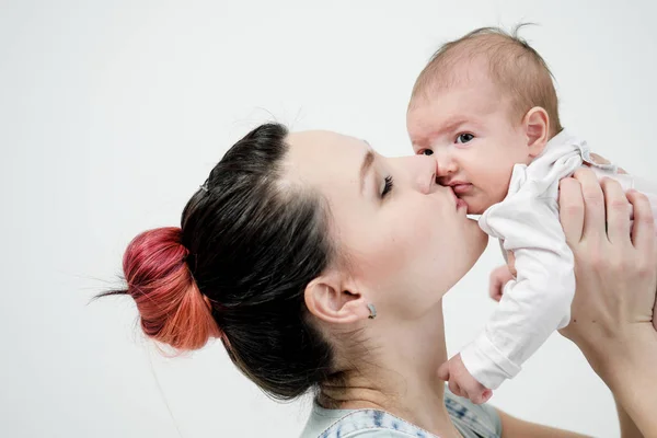 Giovane donna madre in tuta denim tiene un bambino in braccio. Sfondo bianco in studio . — Foto Stock