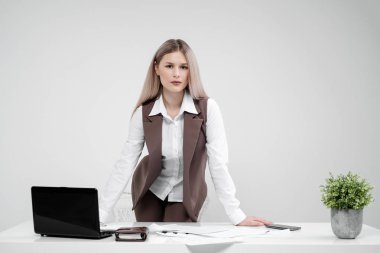 Blonde girl in a business suit works on a computer in a white bright office. clipart