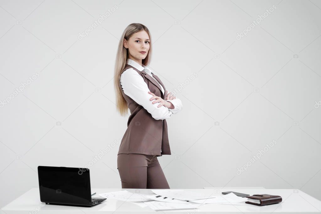 Blonde girl in a business suit works on a computer in a white bright office.