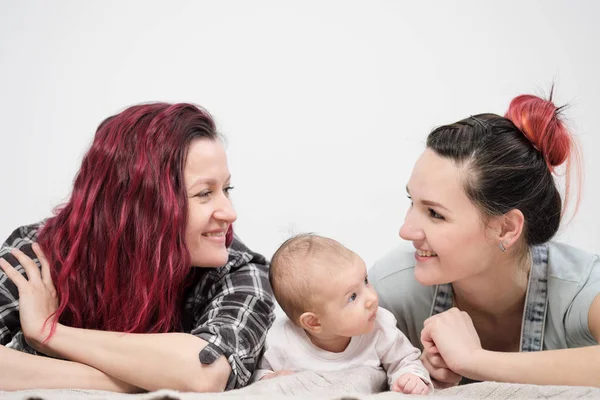 Two young women with a baby on a white background. Same-sex marriage and adoption, homosexual lesbian couple.