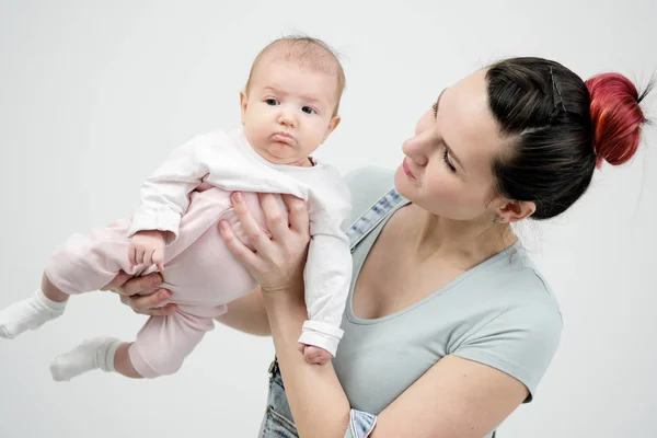 Giovane donna madre in tuta denim tiene un bambino in braccio. Sfondo bianco in studio . — Foto Stock