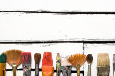 Sanatçılar araçları, üst üste Beyaz ahşap zemin üzerinde boya kirli fırçalar yalan. Kavramsal arka plan metin için yer ile.