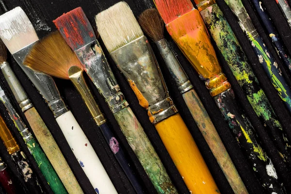 Gli strumenti di artisti, le spazzole in vernice sono in fila su uno sfondo di legno nero . — Foto Stock