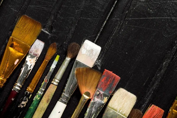Інструменти художника, пензлі в фарбі в ряд на чорному дерев'яному фоні . — стокове фото