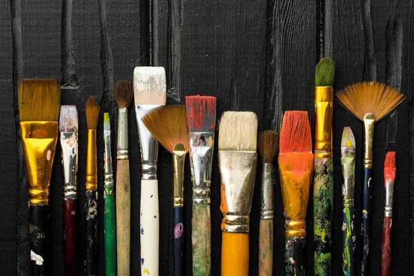 Gli strumenti di artisti, le spazzole in vernice sono in fila su uno sfondo di legno nero . — Foto Stock