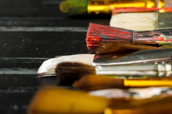 Gli strumenti di artisti, le spazzole in vernice sono in fila su uno sfondo di legno nero . — Foto Stock