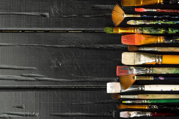 Artistes outils, pinceaux dans la peinture sont dans une rangée sur un fond en bois noir . — Photo