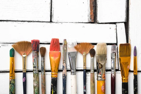 Gli strumenti di artisti, le spazzole sporche in vernice si trovano in fila su uno sfondo di legno bianco. Sfondo concettuale astratto con spazio per il testo . — Foto Stock